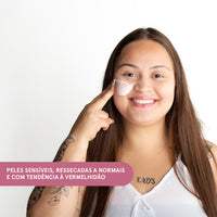 Mulher sorridente com creme no rosto e indicação para peles sensíveis, ressecadas e com tendência à vermelhidão.